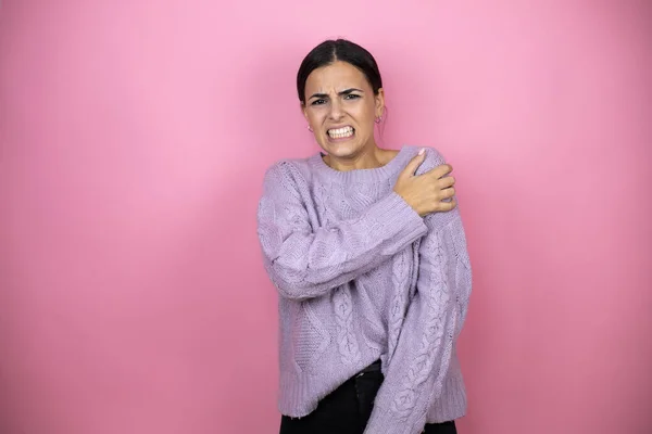 Beautiful woman wearing a casual violet sweater over pink background with pain on her shoulder and a painful expression