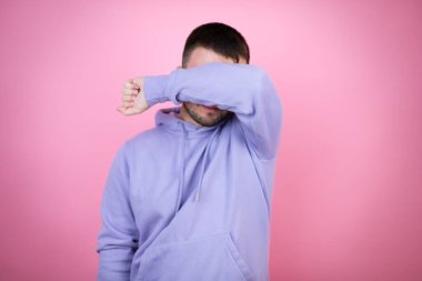 İzole edilmiş pembe arka plan üzerine sıradan bir eşofman üstü giyen genç yakışıklı adam kollarıyla gülen ve komik gözlerle gözlerini kapatıyor. Kör kavram.