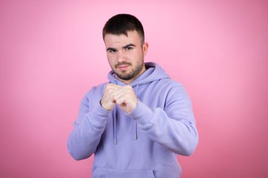 Genç, yakışıklı bir adam pembe arka plan üzerine günlük eşofman üstü giyiyor. Yumruğunu yumrukluyor, saldırıyor, saldırıyor, tehdit ediyor ve şiddet uyguluyor.