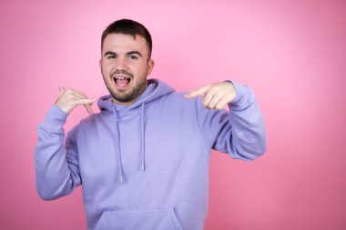 Soyutlanmış pembe arka plan üzerine sıradan bir eşofman giyen genç yakışıklı adam bana elleriyle jest yapıyor.