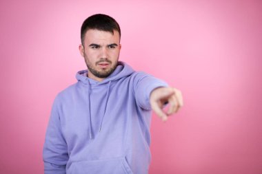 İzole edilmiş pembe arka plan üzerine sıradan bir kazak giyen genç yakışıklı bir adam parmağıyla işaret ederek ileriyi, ağzı açık hayret verici bir ifadeyle, ön tarafta bir şey.