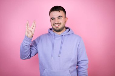 İzole edilmiş pembe arka plan üzerine sıradan bir kazak giyen genç yakışıklı adam Star Trek ucube sembolü yapıyor.