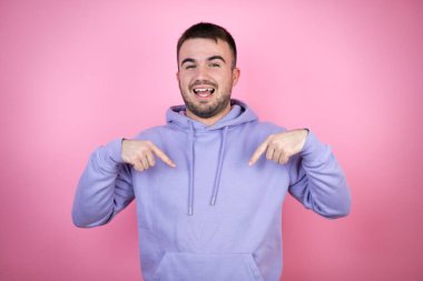Soyutlanmış pembe arka planda rahat bir kazak giyen genç yakışıklı bir adam. Kendine güvenen, yüzünde gülümseme olan, kendini gururlu ve mutlu gösteren bir adam..