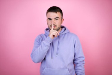 Soyutlanmış pembe arka plan üzerine sıradan bir kazak giyen genç yakışıklı adam sessiz olmak istiyor. Sessizlik ve gizli konsept.