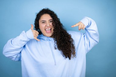 İzole edilmiş mavi arka plan üzerine sıradan bir kazak giyen genç ve güzel bir kadın bana elleriyle jest yapıyor.