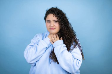 Genç, güzel bir kadın, izole edilmiş mavi arka planda sıradan bir eşofman üstü giyiyor. Ağrılı boynuna dokunuyor. Grip, mantar ve enfeksiyon yüzünden boğazı ağrıyor.