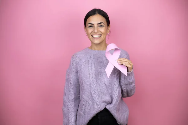 美しいです女性身に着けていますAカジュアルバイオレットセーター上ピンク背景保持A癌リボンで自信を持って笑顔示す歯 — ストック写真