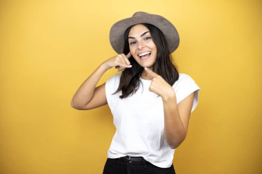 Gayri resmi beyaz tişört ve sarı arka planda duran bir şapka giyen güzel bir kadın elleriyle bana 