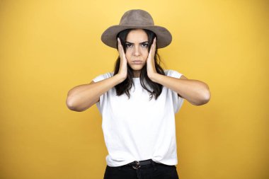 Güzel bir kadın, günlük beyaz tişört ve sarı arka planda duran bir şapka giyer.