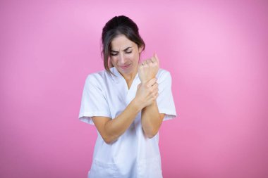 Young brunette doctor girl wearing nurse or surgeon uniform over isolated pink background suffering pain on hands and fingers, arthritis inflammation