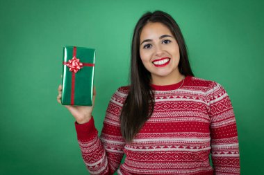 Genç, güzel bir kız hediyesini izole edilmiş beyaz bir arka planda tutuyor. Mutlu bir yüzü var. Kendine güvenen bir gülümsemeyle dişlerini gösteriyor.