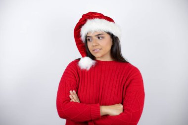 Beyaz arka planda Noel Baba şapkası takan genç ve güzel bir kadın çapraz kollardan sıkılmış ve yorgun göründüğünü düşünüyor.