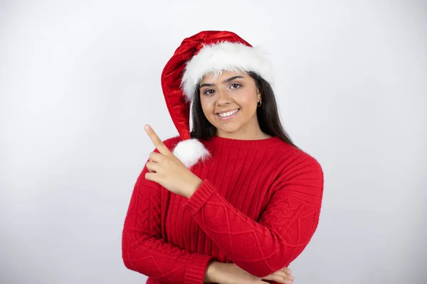 年轻而漂亮的女人 戴着圣诞帽 面带微笑 手指手画脚地朝旁边看去 — 图库照片
