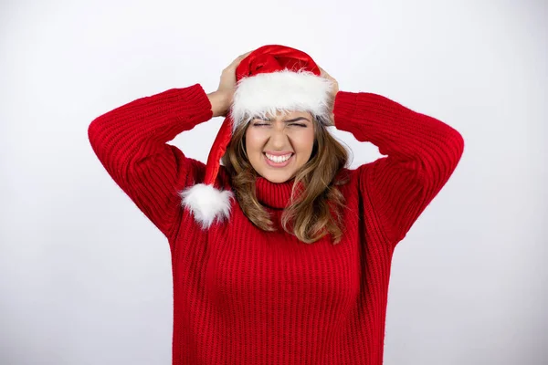Kırmızı bir süveter giyen sarışın genç bir kadın ve beyaz arka planda Noel şapkası takan çaresiz ve stresli bir baş ağrısından muzdarip.