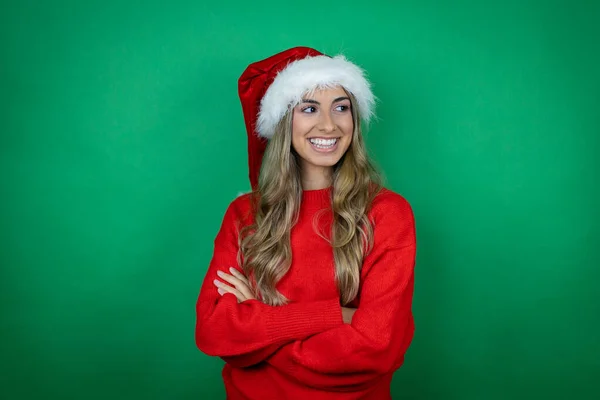 年轻美丽的女孩戴着圣诞圣诞圣诞礼帽 在孤零零的绿色背景上抱着礼物 双手交叉 面带微笑 — 图库照片