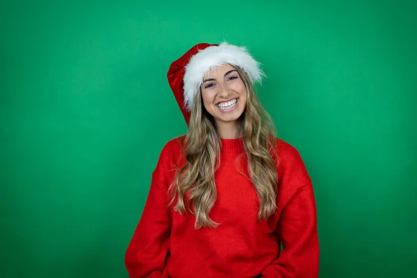 年轻美丽的女孩戴着圣诞圣诞圣诞礼帽 带着礼物披着孤零零的绿色背景 脸上挂着幸福的表情 脸上挂着自信的微笑 露出牙齿 — 图库照片