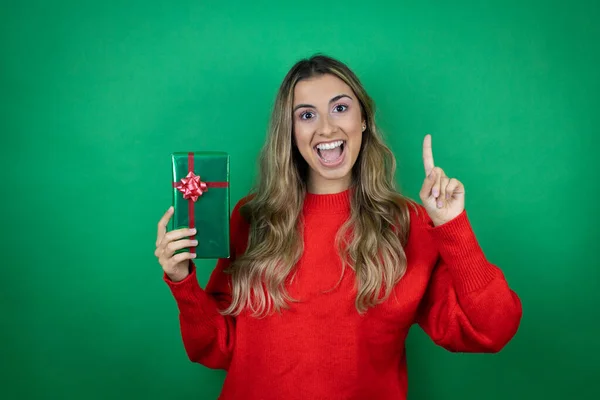 Menina Bonita Jovem Segurando Presente Sobre Fundo Verde Isolado Sorrindo — Fotografia de Stock