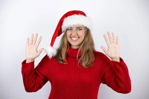 年轻漂亮的金发女人穿着红色休闲装 头戴一顶白色背景的圣诞帽 带着自信和快乐的笑容 用手指指着十号 — 图库照片