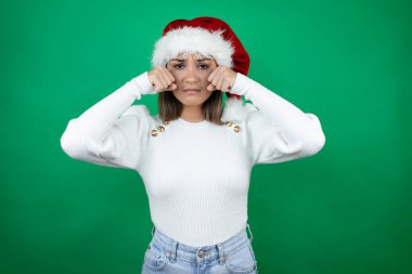 Beyaz arka planda Noel Baba şapkası ve beyaz süveter giyen genç ve güzel bir kadın üzgün ve endişeli, sinirli ve korkmuş. Üzücü ifade.