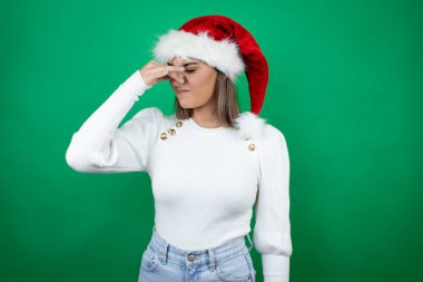Beyaz arka planda Noel Baba şapkası ve beyaz süveter giyen genç bir kadın pis ve iğrenç bir koku alıyor. Dayanılmaz bir koku.