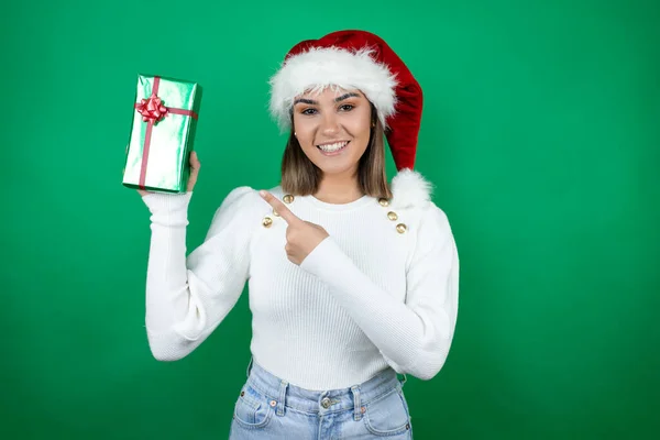 年轻美丽的女人头戴圣诞礼帽 头戴白色背景的白色毛衣 笑容满面 手指手画脚地指向旁边 — 图库照片