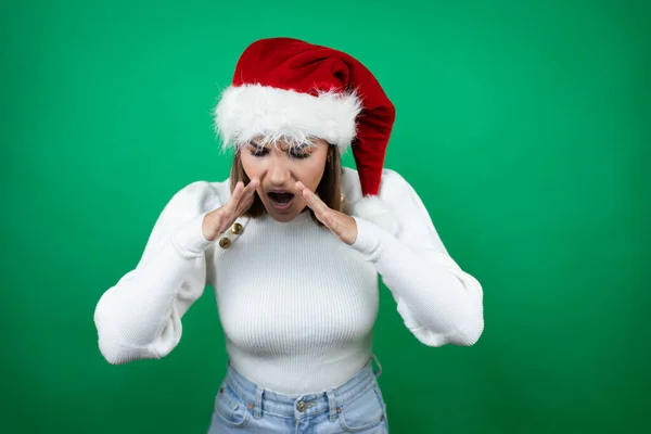 年轻而漂亮的女人 戴着圣诞老人的帽子 穿着白色的毛衣 站在白色的背景上大声喊着 双手捂着嘴大叫着 — 图库照片