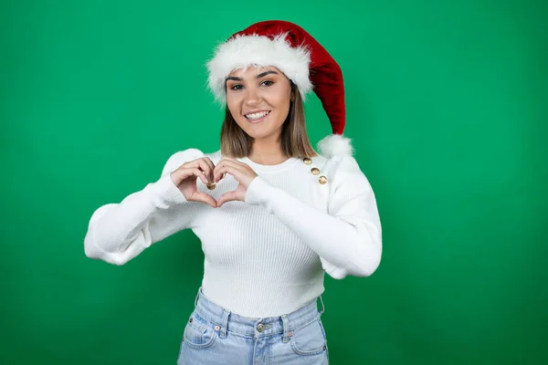 年轻美丽的女人头戴圣诞帽 身穿白色毛衣 背景洁白 带着爱心微笑 双手托着心形 — 图库照片