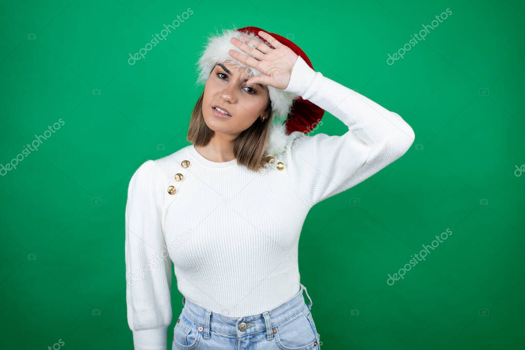 Young beautiful woman wearing a Santa hat and white sweater over white background Touching forehead for illness and fever, flu and cold, virus sick