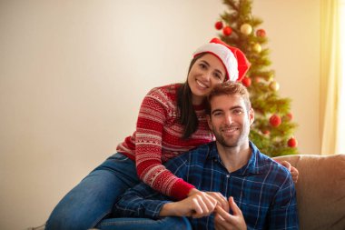 Kanepede genç bir çift, bir noel ağacıyla gülümsüyor ve kendinden emin.