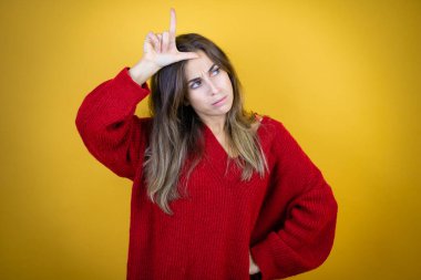 İzole edilmiş sarı arka planda kırmızı süveter giyen genç bir kadın. Alnında parmakları olan insanlarla dalga geçiyor. Ezik hareketler yapıyor, alay ediyor ve hakaret ediyor..