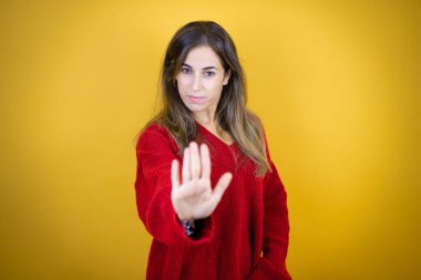 Sarı arka planda kırmızı süveter giyen genç ve güzel bir kadın ciddi ve avucunun içi gibi şarkı söylemeyi kesiyor..