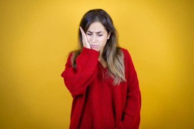 İzole edilmiş sarı arka plan üzerine kırmızı kazak giyen genç bir kadın diş ağrısı ya da diş ağrısı yüzünden ağız ve acı dolu bir ifadeyle dokunuyor.