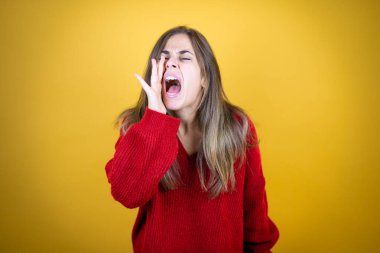 Sarı arka planda kırmızı süveter giyen genç ve güzel bir kadın el pençe divan durup bağırıyor.
