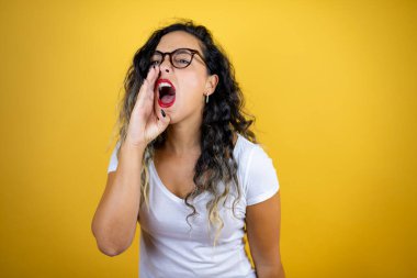 Genç, güzel bir kadın, izole edilmiş sarı arka plan üzerine günlük beyaz tişört giyip el ele tutuşarak bağırıyor ve bağırıyordu.