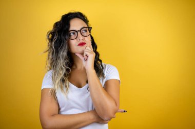 Genç, güzel bir kadın, izole edilmiş sarı arka planda günlük beyaz tişörtler giyip yan tarafa bakıyor.