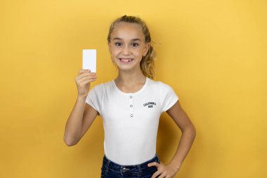 Sarı arka planda duran güzel bir kız çocuğu gülümsüyor ve elinde beyaz bir kart tutuyor.