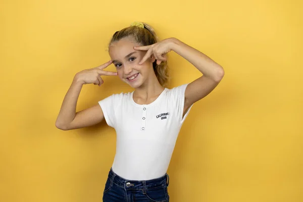 孤立した黄色の背景の上に立つ若い美しい子供の女の子顔の上に指で平和のシンボルを行います 笑顔明るいショーの勝利 — ストック写真
