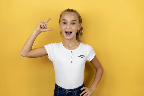 孤立した黄色の背景の上に立つ若い美しい子供の女の子は笑顔と指を見て カメラで小さなサイズの看板を行う手で自信を持ってジェスチャー 概念の測定 — ストック写真