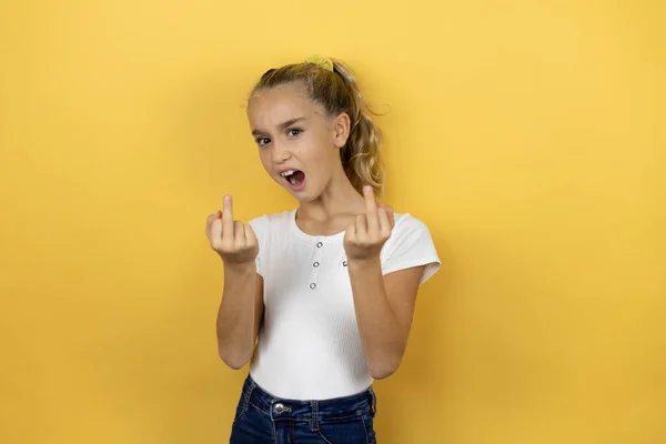 Young beautiful child girl standing over isolated yellow background showing middle finger doing fuck you bad expression, provocation and rude attitude. screaming excited