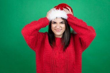 Noel Baba şapkası takan genç ve güzel bir kadın. Yeşil arka plan üzerinde. Baş ağrısı ve stresten muzdarip.