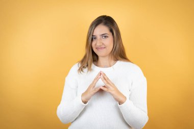 Sarıya boyanmış genç beyaz kadın ellerini birleştirip gülümseyerek gevşemiş ve neşeli gülümsüyor. Başarı ve iyimser