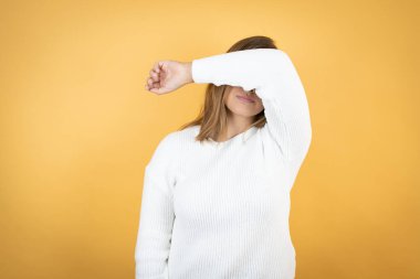 İzole edilmiş sarı arka planda genç beyaz bir kadın. Gözleri kollarıyla kaplıyor. Neşeli ve komik gülüyor. Kör kavram.