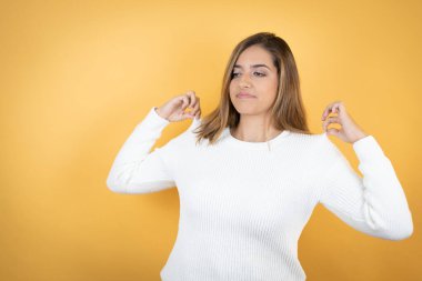 İzole edilmiş sarı arka planı olan beyaz bir kadın tişörtünü başarılı bir ifadeyle tutuyor.