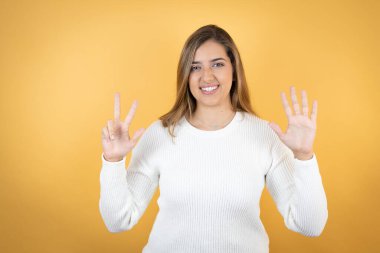 İzole edilmiş sarı arka planda genç beyaz bir kadın sekiz numaralı parmaklarıyla gülümseyerek kendinden emin ve mutlu bir şekilde onu işaret ediyor.