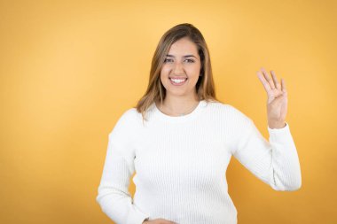 İzole edilmiş sarı arka planda genç beyaz kadın kendini beğenmiş ve mutlu bir şekilde gülümserken dört numarayı işaret ediyor.