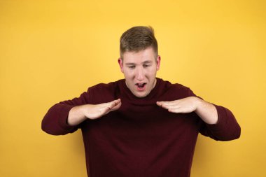 Sarı arka plan üzerine kırmızı süveter giyen genç sarışın adam elleri ağızda bağırıyor ve bağırıyordu.