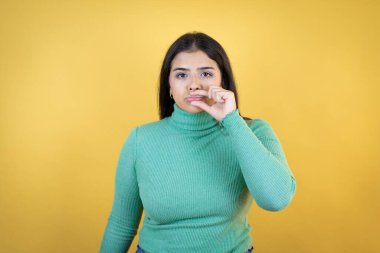 İzole edilmiş sarı arka plan ağzı ve dudakları parmaklarıyla fermuar gibi kapanan beyaz bir kadın. Gizli ve sessiz, tabu konuşması