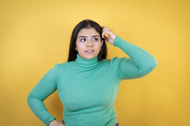 İzole edilmiş sarı arka planı olan beyaz bir kadın soru sorup kafasını karıştırıyor. Şüpheyle karışık, kafa kafaya düşünerek.