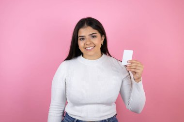 Soyutlanmış pembe arka planda güzel bir kadın gülümsüyor ve elinde beyaz bir kart tutuyor.