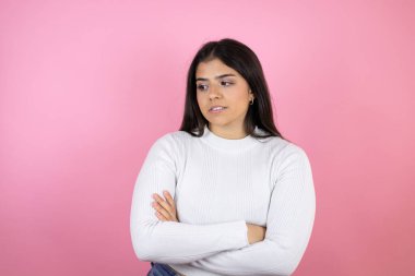 Soyutlanmış pembe arka planı olan genç ve güzel bir kadın çapraz kollardan sıkılmış ve yorgun göründüğünü düşünüyor.